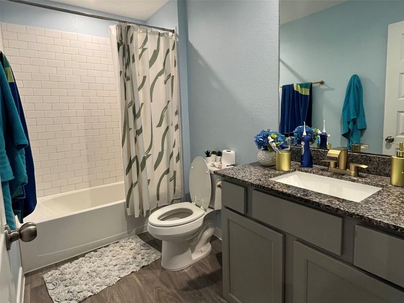 This bathroom features a clean, modern design with a granite countertop and brass fixtures. It includes a bathtub with a tiled shower, a large mirror.