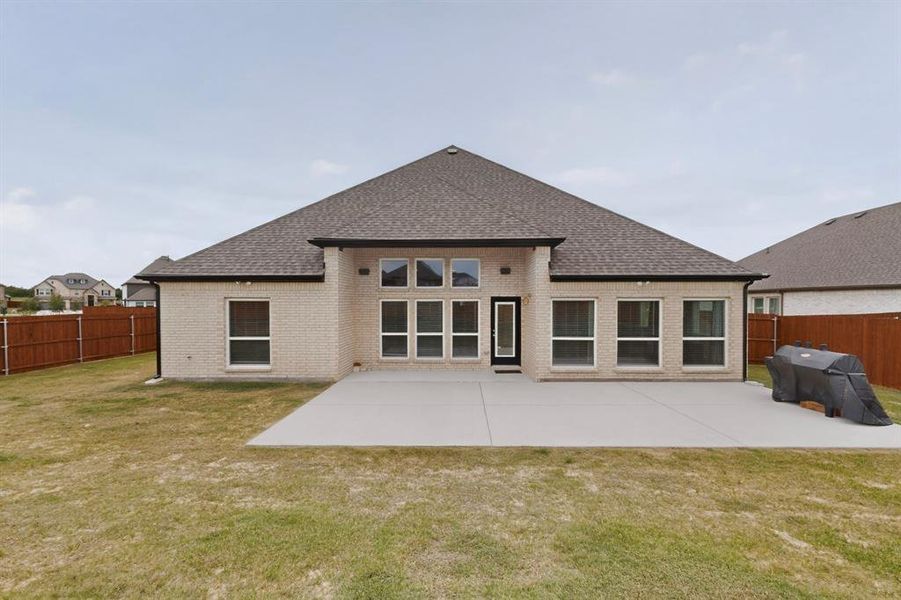 Rear exterior featuring light-colored brick, a dark shingle roof, and a concrete patio Rear exterior featuring light-colored brick, a dark shingle roof, and a concrete patio