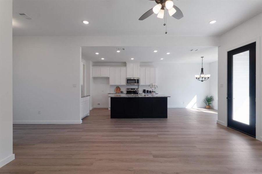 Kitchen with white cabinets, a kitchen island with sink, decorative light fixtures, stainless steel appliances, and light hardwood / wood-style floors