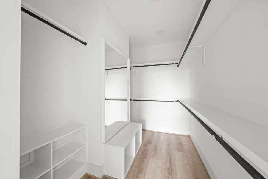Conveniently connected to the primary bathroom, the walk-in closet offers an organized retreat featuring custom hanging shelves and dedicated shoe storage. A large mirror with bench makes the perfect dressing area. Conveniently connected to the primary bathroom, the walk-in closet offers an organized retreat featuring custom hanging shelves and dedicated shoe storage. A large mirror with bench makes the perfect dressing area.