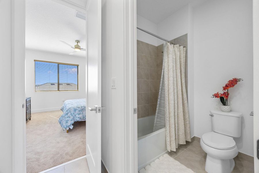 Ensuite bathroom with shower / bathtub combination with curtain, light tile patterned flooring, ceiling fan, and light carpet