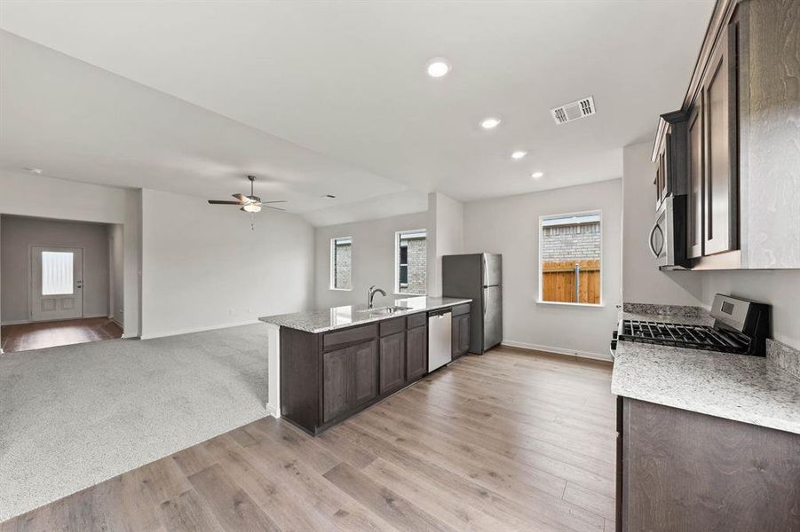 Kitchen featuring dark brown cabinetry, light stone counters, stainless steel appliances, open floor plan, and recessed lighting Kitchen featuring dark brown cabinetry, light stone counters, stainless steel appliances, open floor plan, and recessed lighting