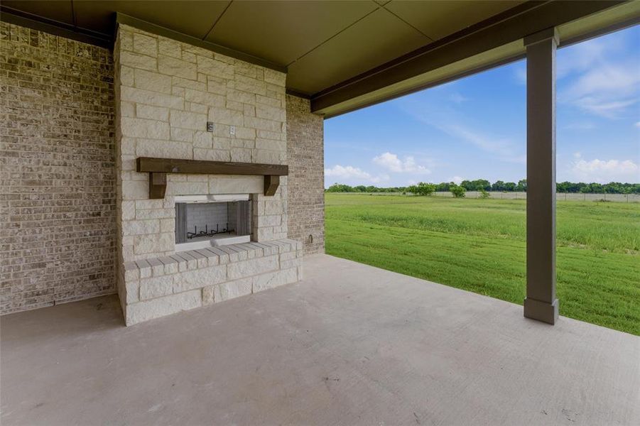 Covered patio featuring an outdoor fireplace with stone surround, a wood mantel, and a concrete floor