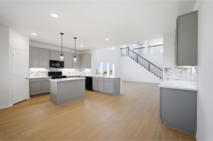 Kitchen featuring gray cabinets, a kitchen island, tasteful backsplash, black appliances, and light wood-style floors