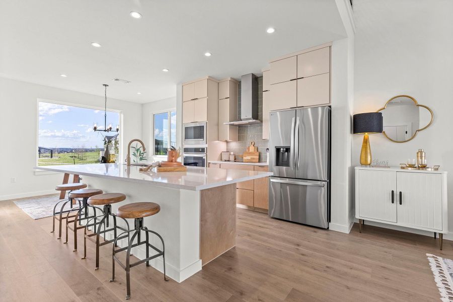 Kitchen featuring stainless steel appliances, a breakfast bar, suspended lighting, light wood-style floors, and dual tone cabinets
