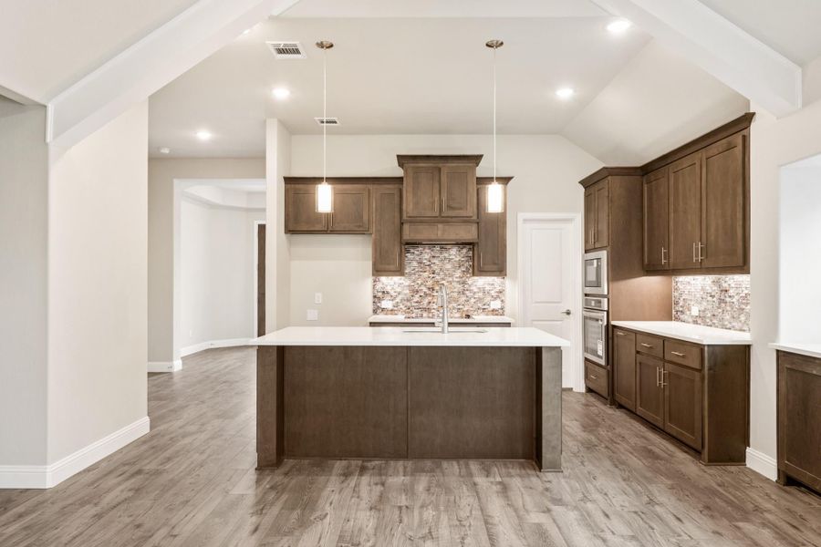 Kitchen with dark wood cabinets, center island, tile backsplash, and hardwood floors under vaulted ceiling