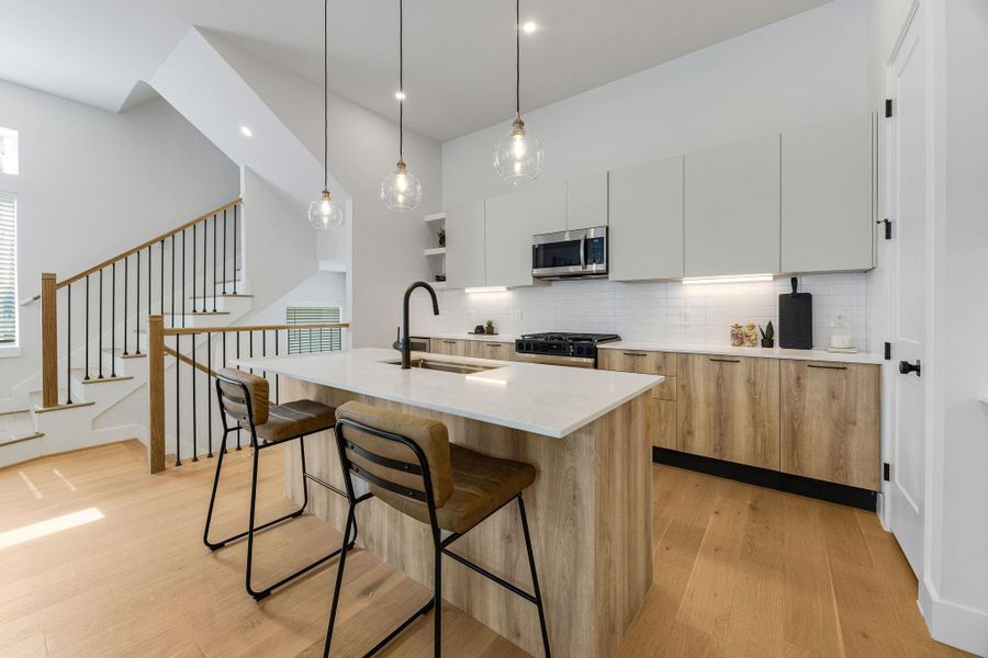 Stunning modern kitchen featuring a large waterfall-style island, quartz countertops, custom cabinetry, designer pendant lighting, stainless steel appliances, and warm wood accents in this luxury Independence Heights home.