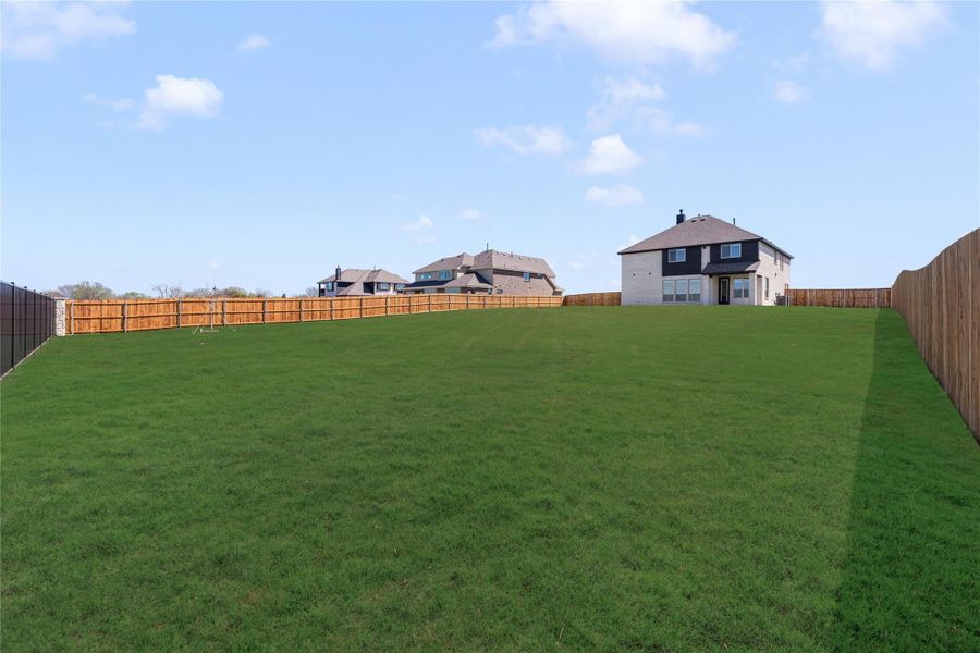 Large fenced backyard with green grass and two-story home visible in the background Large fenced backyard with green grass and two-story home visible in the background