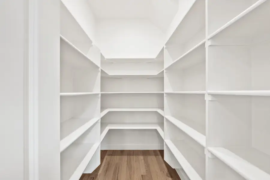 Walk-in pantry with white built-in shelves on three walls and hardwood floors
