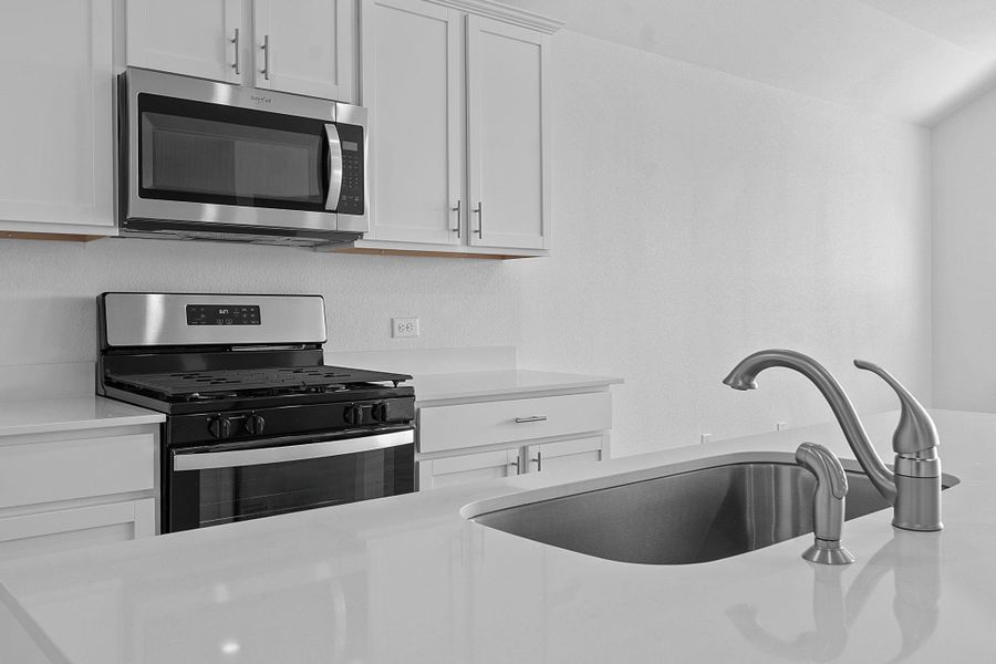 Kitchen featuring stainless steel appliances, white cabinets, and light stone countertops