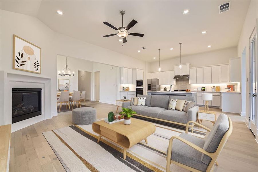 Virtually Staged - Living area featuring light wood-type flooring, recessed lighting, a glass covered fireplace, a ceiling fan, and a chandelier