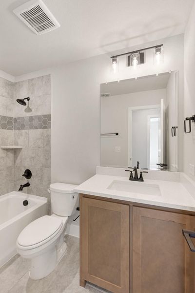 Bathroom with wood vanity, white quartz countertop, tub-shower combo with gray tile, and black fixtures