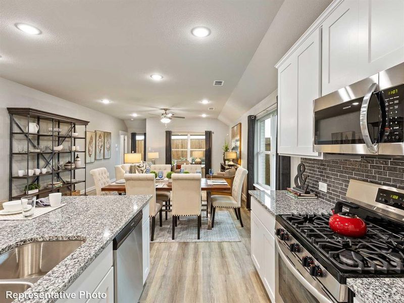 Modern kitchen featuring granite countertops, stainless steel appliances, white cabinetry, and subway tile backsplash