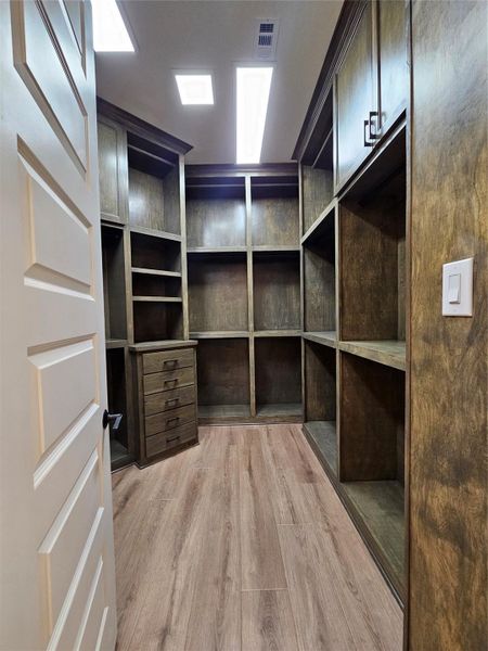 This photo shows a spacious walk-in closet with rich wooden shelving and ample storage, including multiple drawers and open compartments. The room is well-lit with recessed lighting, highlighting the elegant wood grain and providing a luxurious feel.