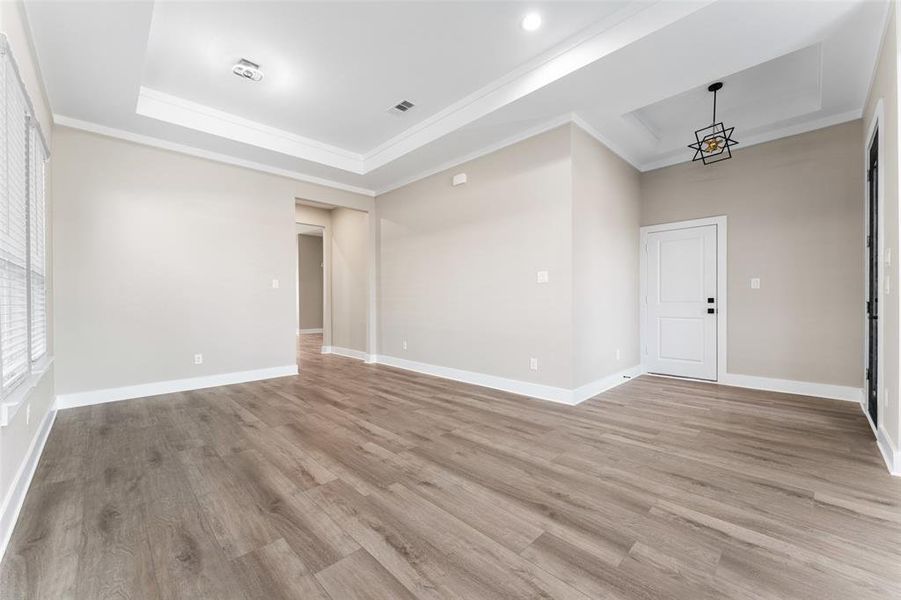 Unfurnished room featuring ornamental molding, a raised ceiling, light hardwood / wood-style flooring, and a notable chandelier