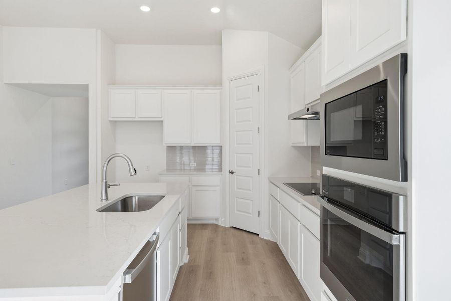 Kitchen featuring appliances with stainless steel finishes, light wood finished floors, white cabinetry, a kitchen island with sink, and decorative backsplash Kitchen featuring appliances with stainless steel finishes, light wood finished floors, white cabinetry, a kitchen island with sink, and decorative backsplash