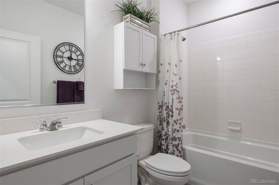 Full bath with modern fixtures, white cabinetry, quartz counters, and a tiled tub/shower combination.