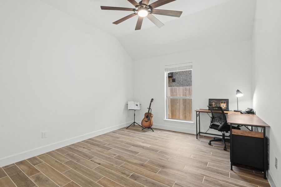 This secondary bedroom complete with an ensuite bathroom, features a modern design with wood-look tile flooring, a ceiling fan, and ample natural light from the large window.