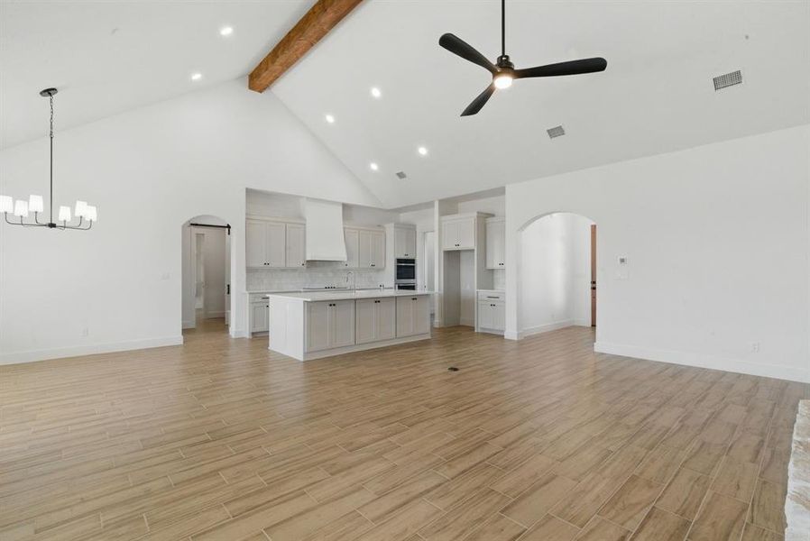 Unfurnished living room featuring arched walkways, beam ceiling, high vaulted ceiling, light wood finished floors, and ceiling fan Unfurnished living room featuring arched walkways, beam ceiling, high vaulted ceiling, light wood finished floors, and ceiling fan