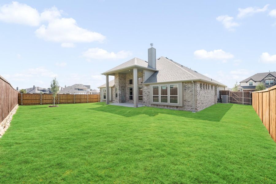 Backyard of two-story brick home with large green lawn, covered patio, and wood privacy fence Backyard of two-story brick home with large green lawn, covered patio, and wood privacy fence