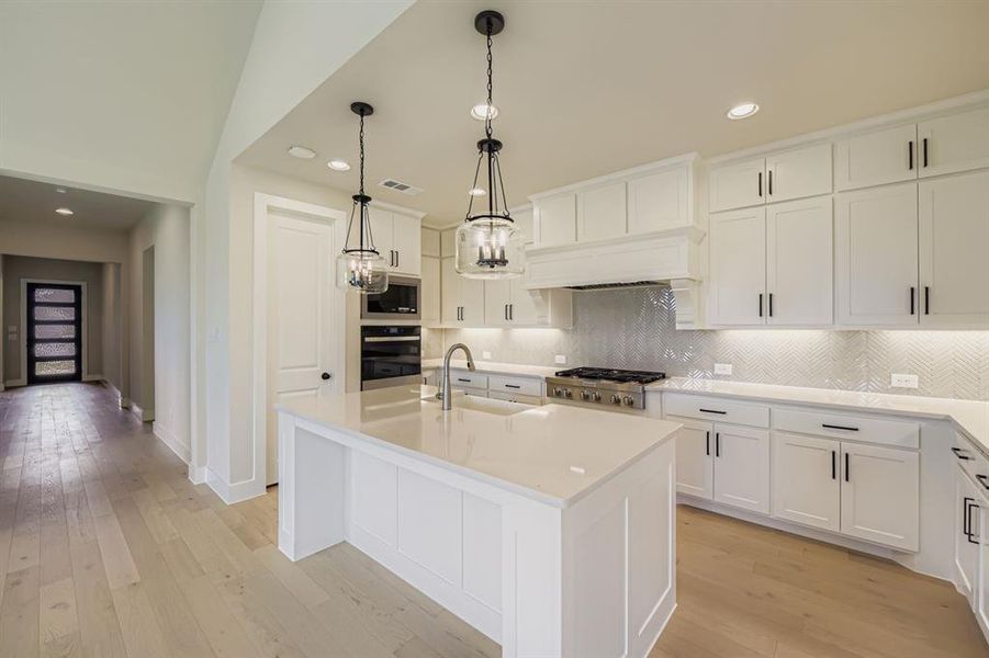 Kitchen featuring backsplash, light wood-style flooring, recessed lighting, an island with sink, and pendant lighting