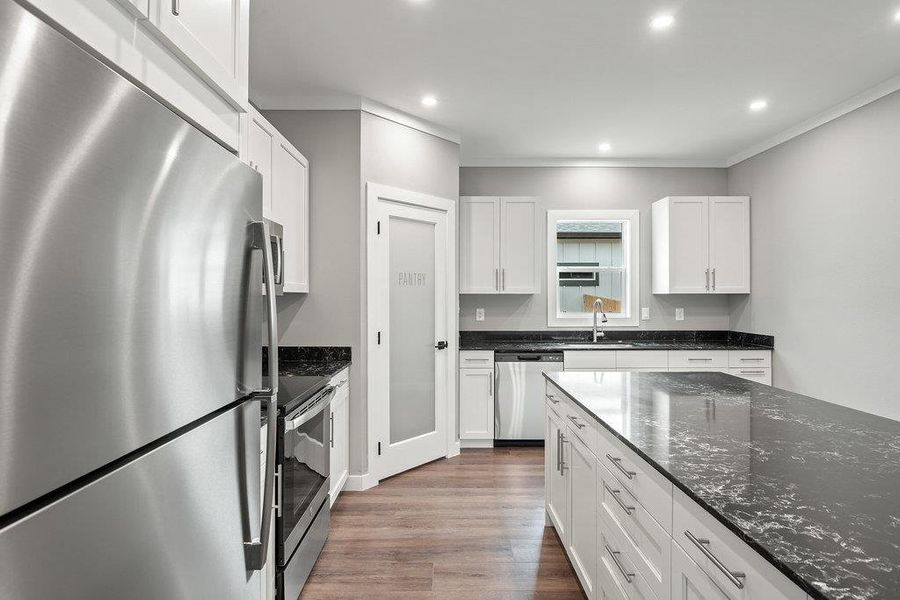 Kitchen featuring stainless steel appliances, dark stone countertops, white cabinets, dark wood-style flooring, and ornamental molding