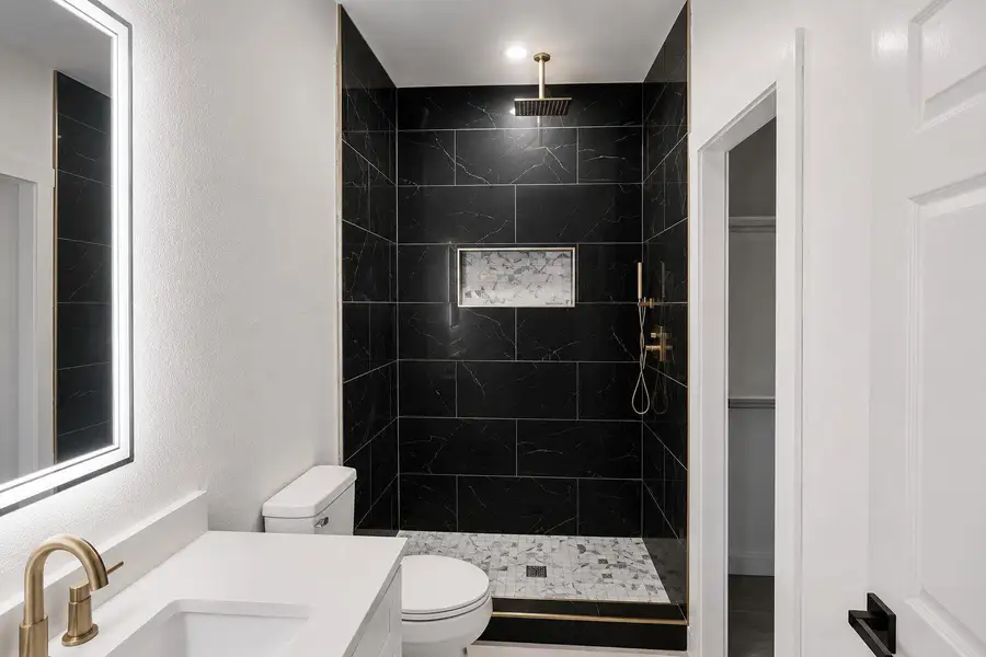 Luxurious black marble shower features a niche and elegant gold fixtures.