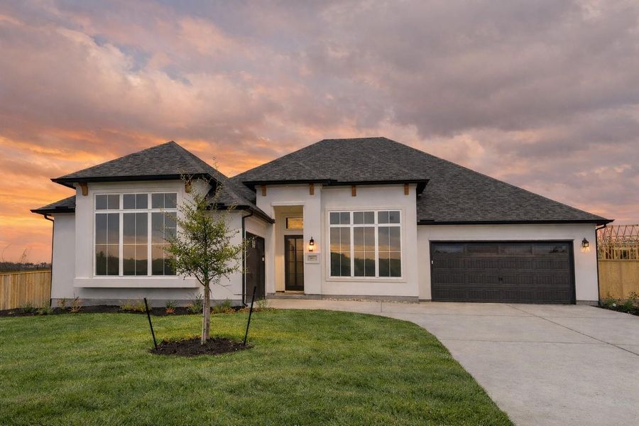 View of front facade featuring a garage, driveway, a shingled roof, and stucco siding