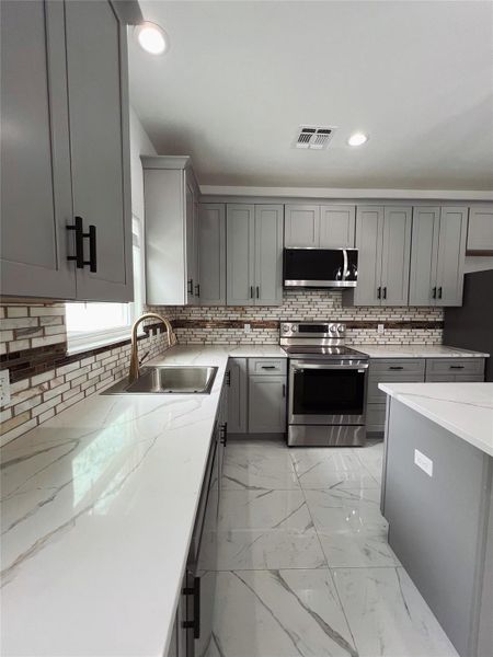 Kitchen featuring gray cabinets, stainless steel appliances, visible vents, and a sink Kitchen featuring gray cabinets, stainless steel appliances, visible vents, and a sink