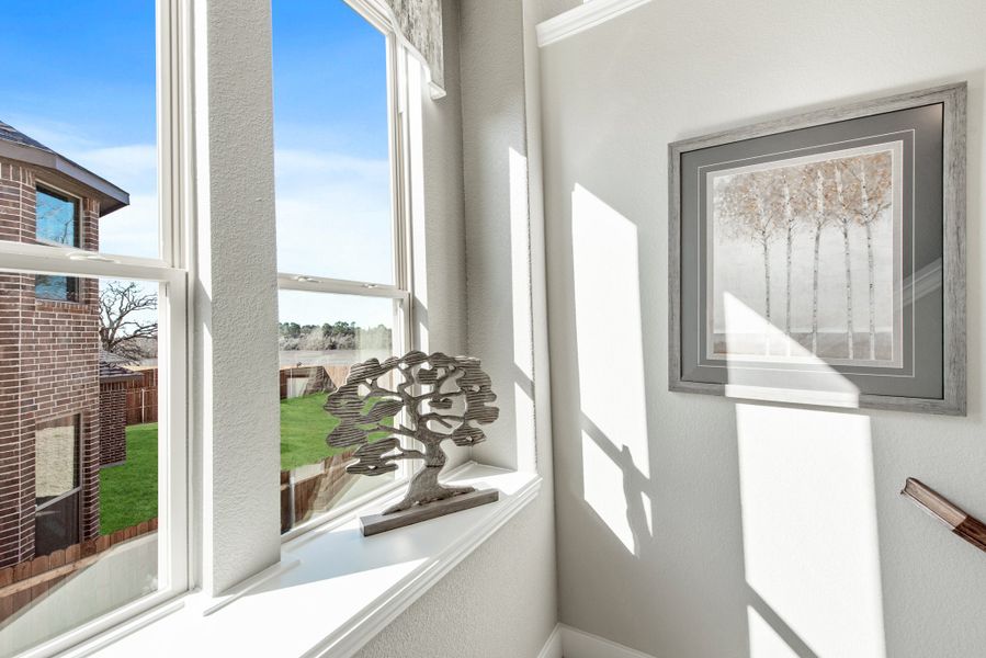 Bright stairway landing with large window, tree sculpture on sill, and framed wall art overlooking backyard