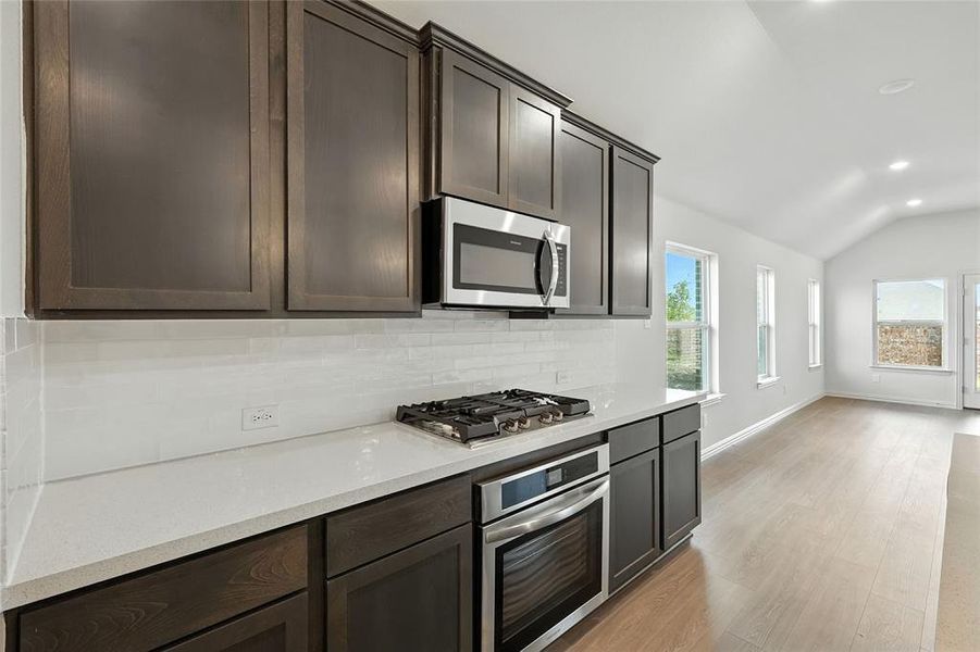 Kitchen with dark brown cabinets, recessed lighting, stainless steel appliances, light stone counters, and backsplash Kitchen with dark brown cabinets, recessed lighting, stainless steel appliances, light stone counters, and backsplash