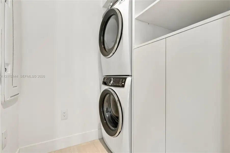 Laundry area featuring a stackable front-load washer and dryer, integrated white cabinetry with open shelving, and light-toned flooring
