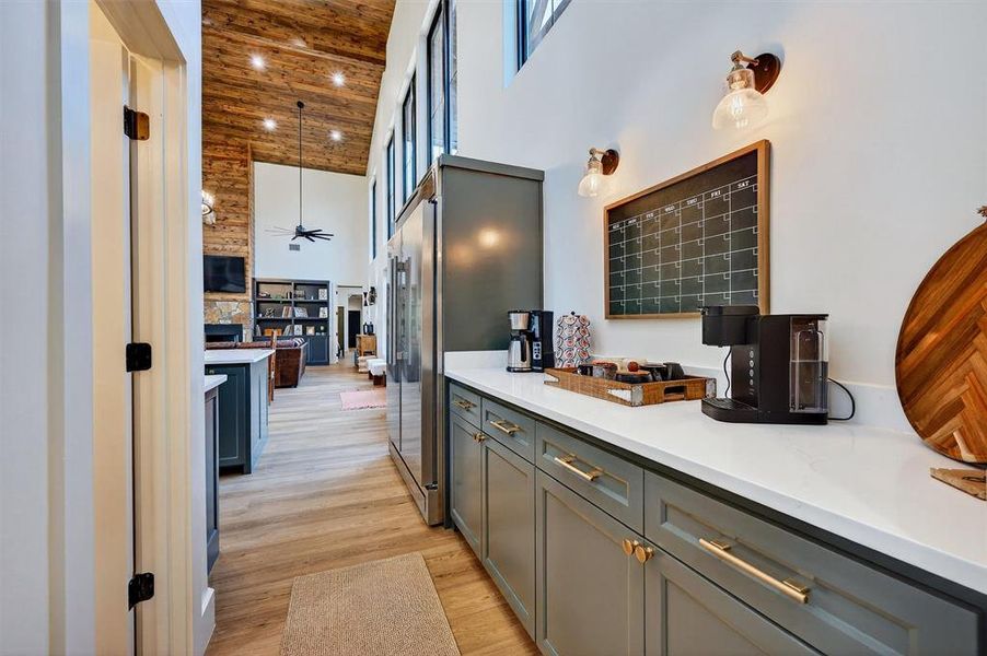 Kitchen with a towering ceiling, light wood-style floors, hanging light fixtures, light stone counters, and high quality fridge Kitchen with a towering ceiling, light wood-style floors, hanging light fixtures, light stone counters, and high quality fridge
