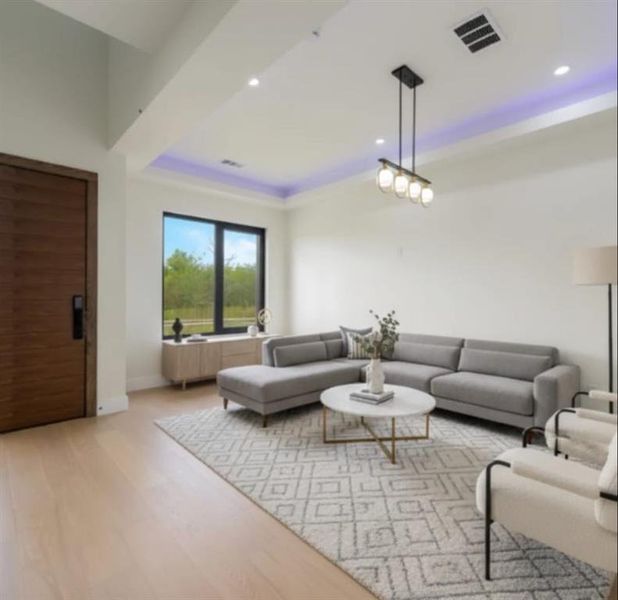 Living room with light wood finished floors, a raised ceiling, and recessed lighting