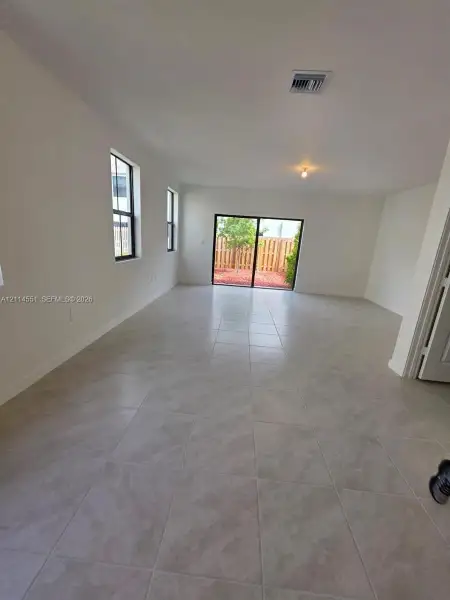 Open-concept interior featuring large-format neutral tile flooring, dual-pane windows with dark frames, and a sliding glass door