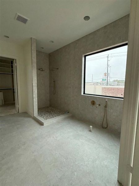 Primary Bathroom- Large-format tiles, textured wall tile, dual shower heads, pebble mosaic floor, and brushed gold fixtures. Closet access visible at left. (Construction Photo as of 3/8/26 - Edited)