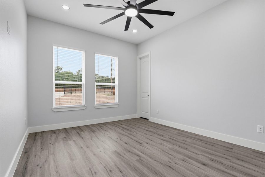 Spacious room with wood-finish flooring, two large windows with blinds, a ceiling fan with integrated lighting, and recessed ceiling lights