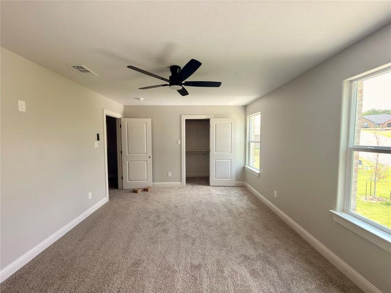 Spacious interior room featuring neutral wall paint, plush carpeting, a modern ceiling fan, and multiple windows providing natural illumination