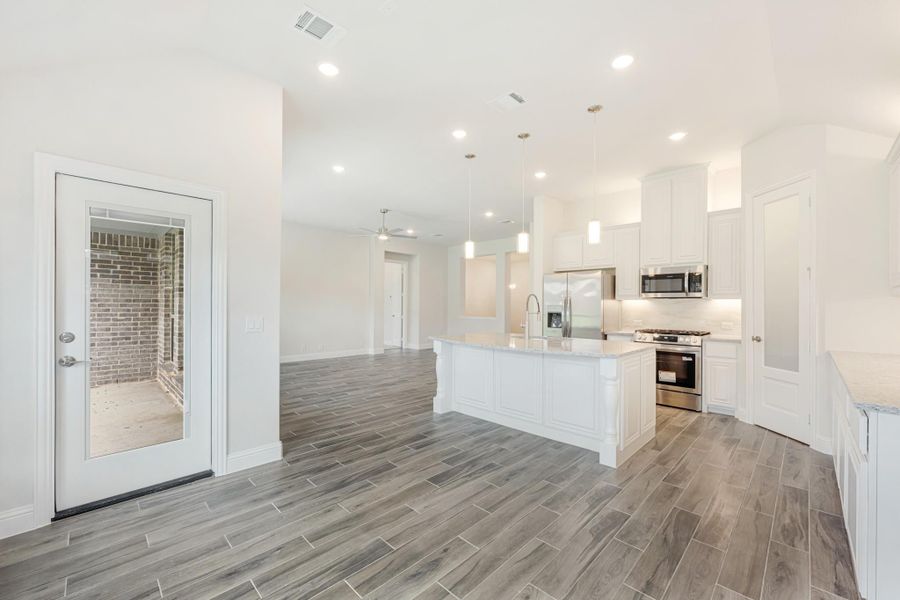 Open kitchen with white cabinets, center island, stainless steel appliances, and wood-look tile floors