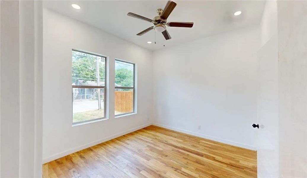 Bright interior space featuring wood-finish flooring, two large windows, a ceiling fan with integrated lighting, and recessed ceiling lights