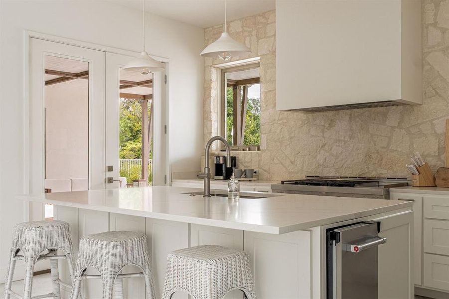Kitchen with decorative light fixtures, a breakfast bar area, white cabinets, a kitchen island with sink, and concrete floors Kitchen with decorative light fixtures, a breakfast bar area, white cabinets, a kitchen island with sink, and concrete floors