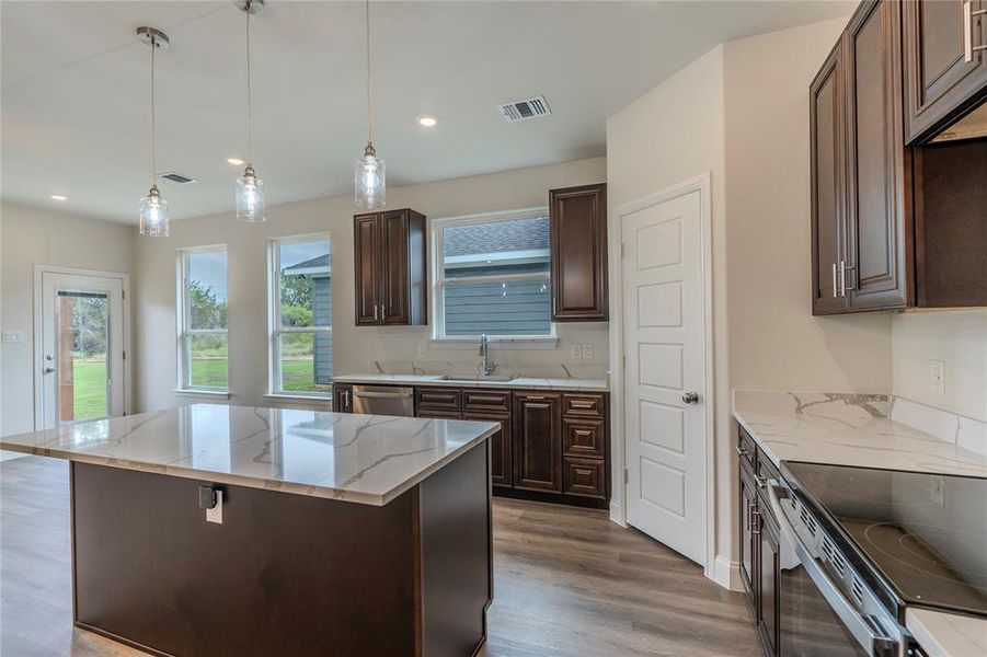 Kitchen with pendant lighting, wood-type flooring, light stone counters, and sink