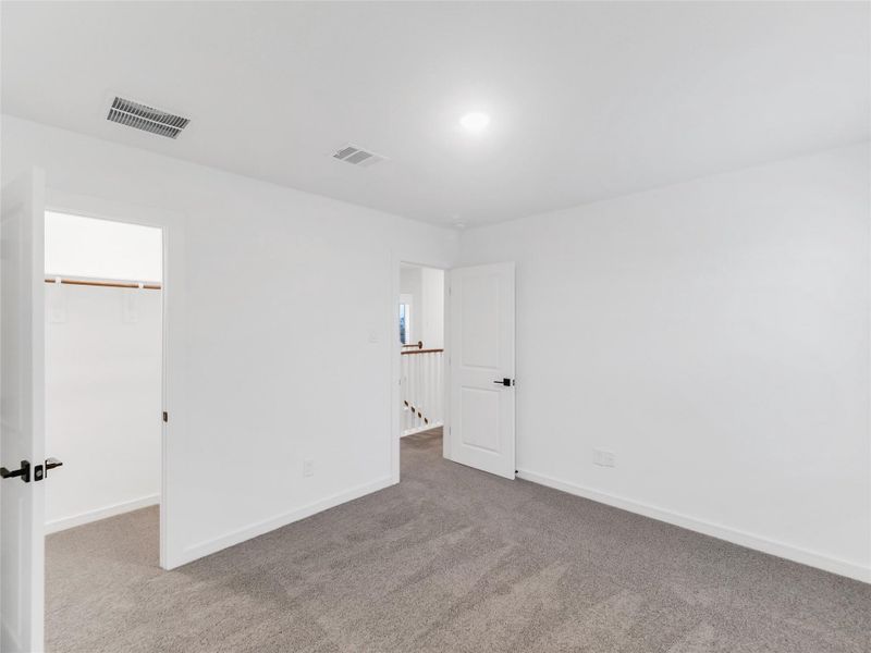 third bedroom with carpeted flooring. It features a walk-in closet on the left and a doorway leading to a hallway. The room is well-lit with a ceiling light.