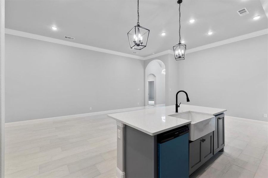 Kitchen with a center island with sink, stainless steel dishwasher, ornamental molding, pendant lighting, and sink