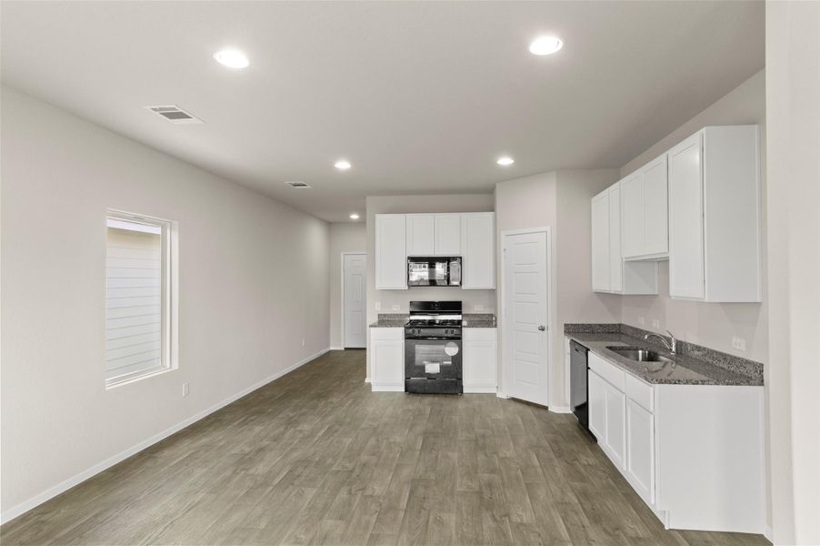 Kitchen featuring black appliances, wood finished floors, recessed lighting, white cabinets, and dark stone counters