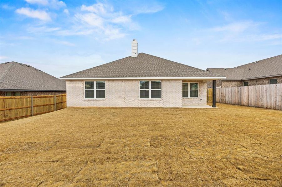 Rear view of house featuring a chimney, a patio, roof with shingles, and a fenced backyard
