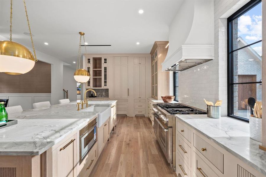 The kitchen features a large island with a farmhouse sink and brass fixtures, light wood flooring, and extensive cabinetry