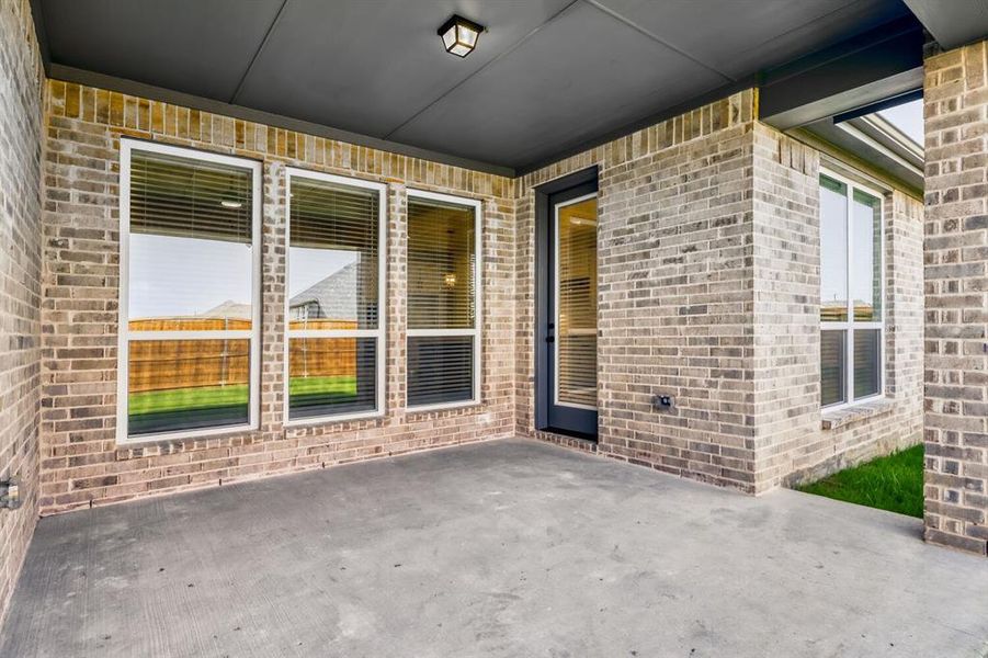 Covered concrete patio with a dark ceiling and recessed lighting, featuring a brick exterior wall