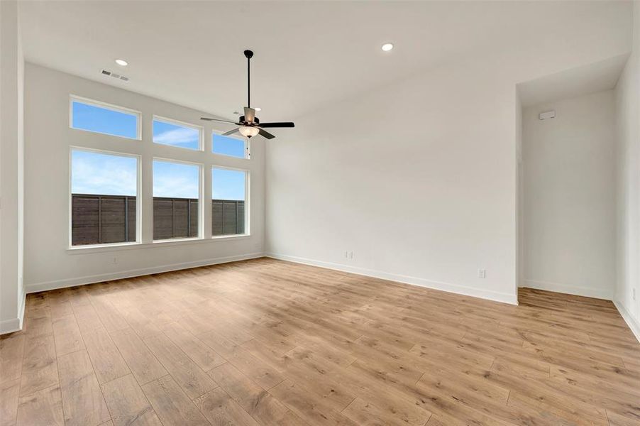 Spacious interior room featuring high ceilings, wood-finish flooring, a contemporary ceiling fan, recessed lighting, and a wall of windows