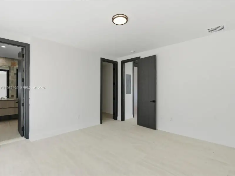 Neutral-toned stone-finish flooring, dark-stained interior doors, matte black door hardware, and a minimalist flush-mount ceiling fixture Neutral-toned stone-finish flooring, dark-stained interior doors, matte black door hardware, and a minimalist flush-mount ceiling fixture